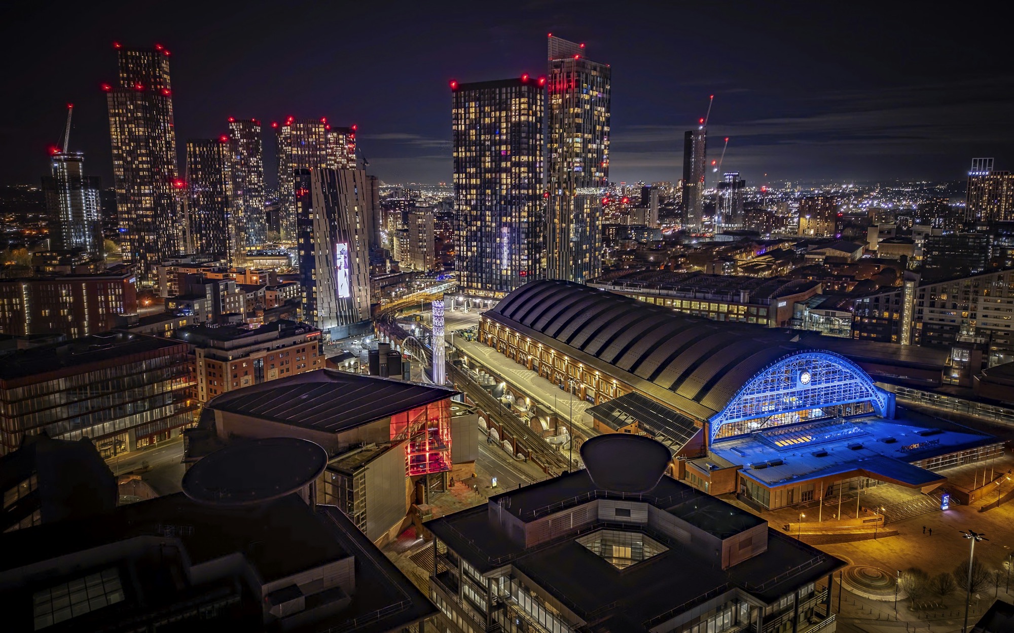 Manchester’s skyline at night, with the lit arched roof of Manchester Central in front of the Deansgate Square towers